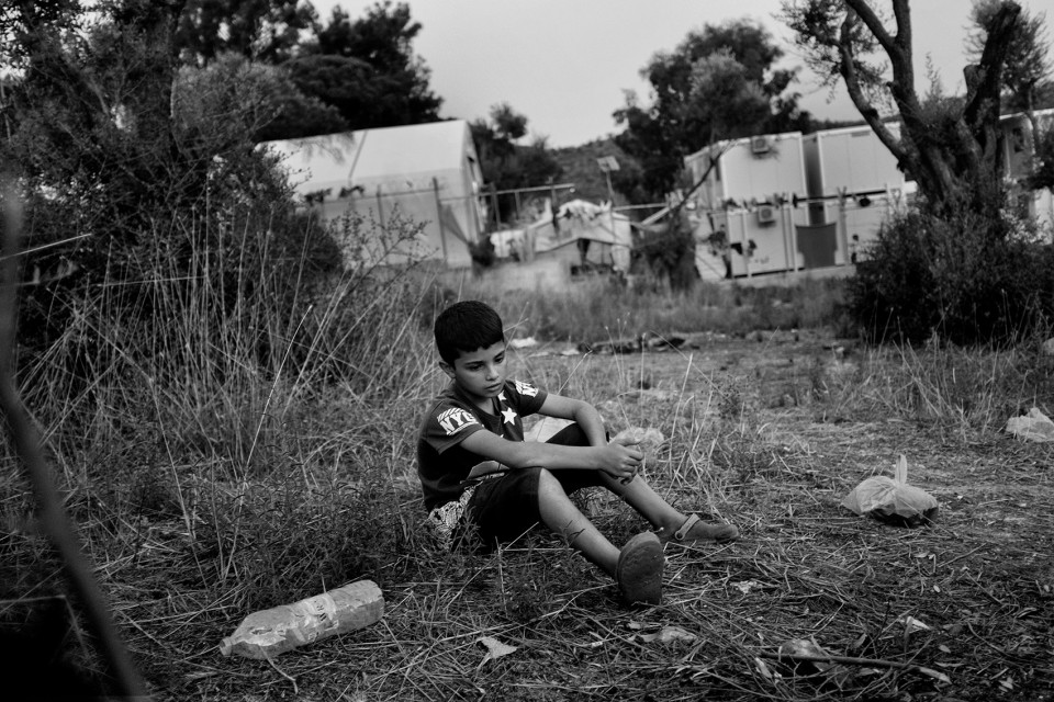 A Syrian young boy who came with his parents and 2 sisters just outside the back of the refugee camp Moria where they prepare their dinner on a wood fire. Lesbos, Greece